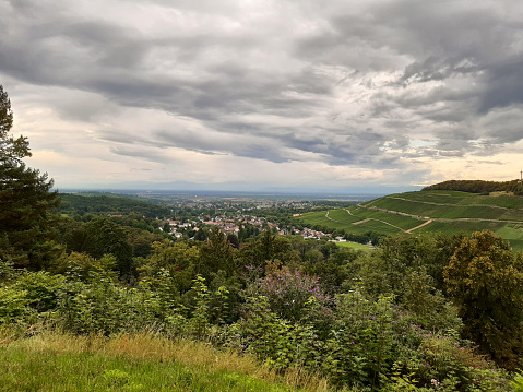 View towards Römerberg with its vineyards and a village, Markgräflerland. View towards Rhine on a cloudy day, Vogese mountains on horizon.