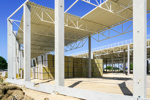 Reinforced concrete supports, steel frame structure, corrugated metal roof and thermal insulating materials stacks of unfinished commercial building