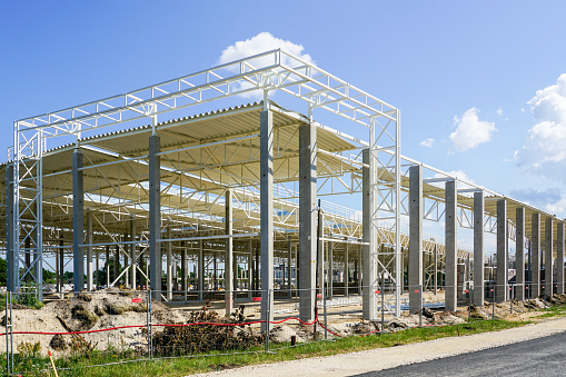 Unfinished large warehouse steel frame structure on reinforced concrete supports with corrugated steel roof, blue sky background