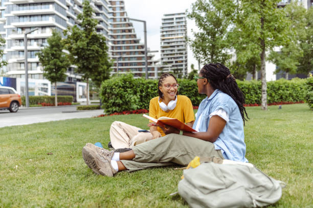 istock Two young female students sitting on a grass area and cheerfully discussing a book together 1676822683