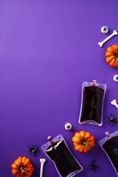 istock Happy Halloween holiday vertical flat lay composition with decorations, blood packets, pumpkins, eyes, bones on purple background. Top view. 1676833127