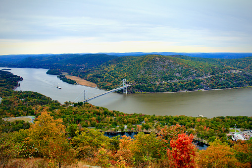 Bear Mountain Bridge in Autumn is a photograph taken just before dusk on a warm and overcast day in early Autumn looking East over the Hudson River and Bear Mountain as a barge is being towed.