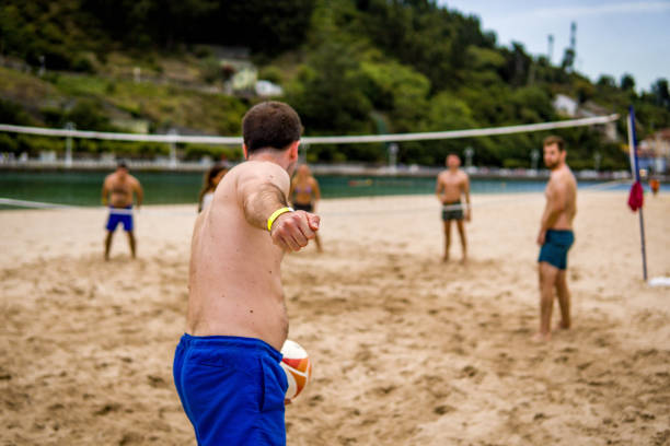 niño sin camisa preparado para servir y golpear la pelota con su brazo derecho hacia la red en un partido de voleibol de playa con amigos - volley kick fotografías e imágenes de stock