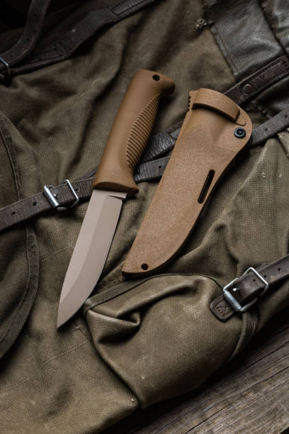 istock Modern knife with rubberized handle and plastic sheath. Cold steel lies on a vintage hiking backpack. Wooden background. 1676879703