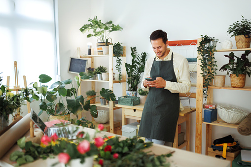 Young handsome man using phone at his flower shop