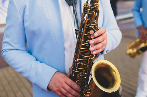 Concert view of saxophonist in a blue and white suit, saxophone sax player with vocalist and musical band during jazz orchestra show performing music on stage in the scene lights