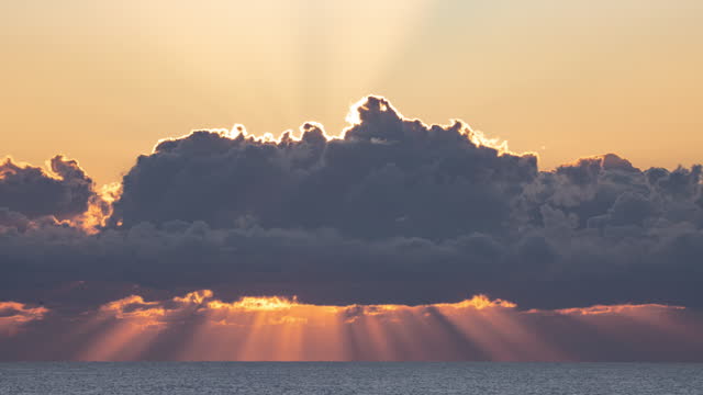 Timelapse of sun rays through moving clouds as the sun rises over the pacific ocean