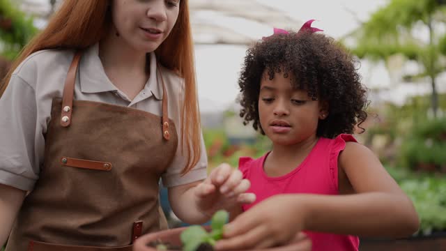 Saleswoman teaching a girl to plant in a garden center