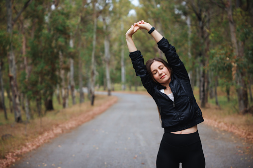 Women exercising. Healthy young woman warming up outdoors. She is stretching her arms and looking away. Young fitness sport woman running on the road in the morning