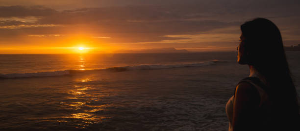 istock Young woman backlit against the sea at sunset using the phone. Space for text. 1676968165