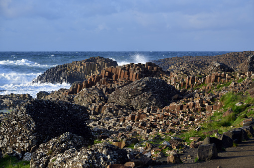 Bushmills, County Antrim, Northern Ireland / Ulster: Giant's Causeway and the Atlantic - eroded hexagonal basalt columns entering the ocean - This area was mainly chalk when enormous amounts of highly fluid lava came to the surface from the depths some 60 million years ago. The constructive continental plate movement created rifts and oceanic spreading or sea floor spreading. This created a thick lava plateau. This lava cooled and shrank, so we still see the characteristic basalt columns today - UNESCO World Heritage Site 'The Giant's Causeway and Causeway Coast'