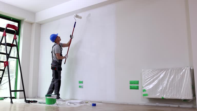 Man master paint ceiling with white paint roller in room