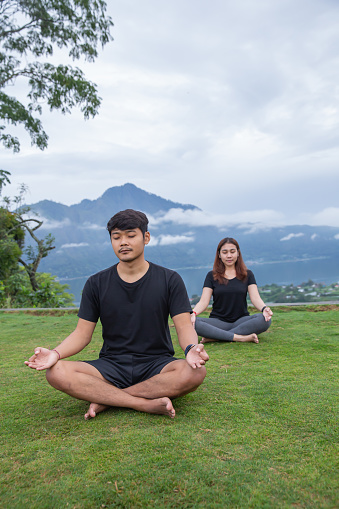 Close-up shot of two friends meditating together in the backyard with a mountain view  background
