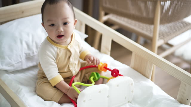 Baby Boy Playing a Colorful Toys on Baby Bed in Bedroom at Home