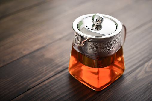 Glass teapot  with  metal cover on wooden backgroud closeup