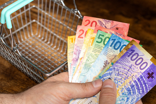 Switzerland money, a bundle of francs held in hand against the backdrop of an empty shopping cart, financial concept