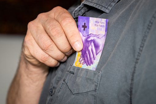 The man takes a thousand Swiss francs out of his shirt's pocket, the highest denomination of paper money in Switzerland, business concept, 1000 francs banknote