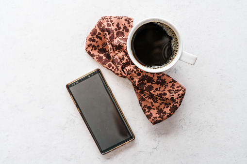 A flatlay of a cup of coffee, a phone, and a pink floral hairbow in Iowa City, Iowa, United States