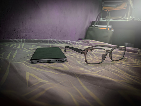 glasses and smartphone on the bed, shot from the front, purple color theme