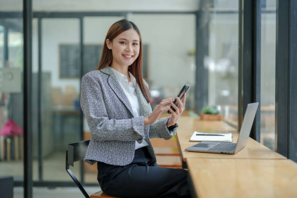istock Charming Asian woman with a smile sits with a smartphone answering a chat perform financial transactions via mobile, play various social media at the office. 1677299614