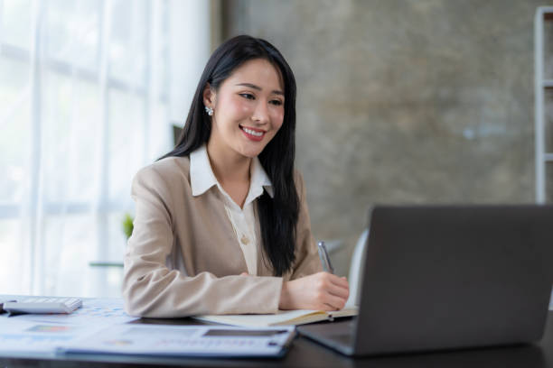 istock Beautiful Asian business woman using her laptop to work and enjoy working, taking note, reviewing assignment and smiling in the office. 1677300135