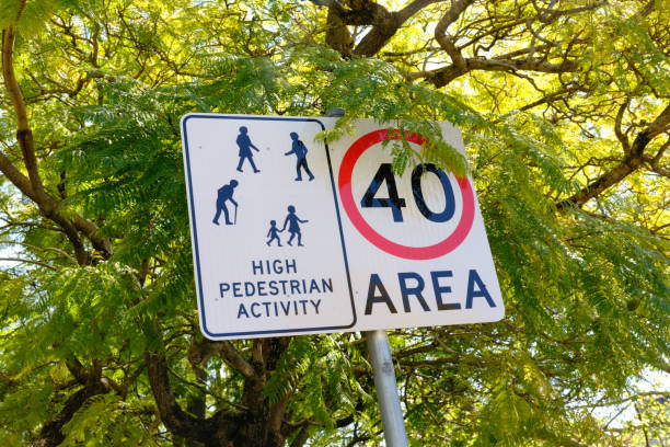 Speed limit and high pedestrian activity zone sign on a pole Speed limit street sign partially hidden by a large tree. speed limit sign australia stock pictures, royalty-free photos & images