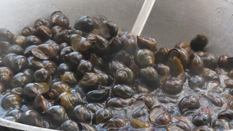 close up of a woman turning over boiling snails inside a wok