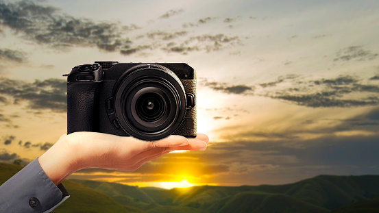 Human hand holding camera with a blue sky background. World Photography Day