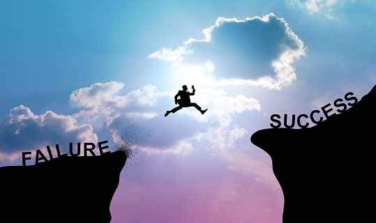 Silhouette of businessman leaping or jumping across two cliffs. Business concepts of decision-making, courage, and risk-taking for success.