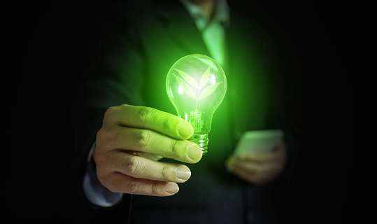 A hand of a businessman holding light bulb with leafs and light. The idea concept with innovation and inspiration for an environmentally friendly or green businesses.