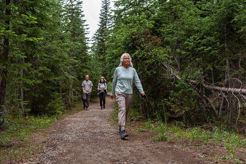 Active and healthy senior woman of Pacific Islander descent leads her multiracial multigenerational family on a hike through a forest in the Pacific Northwest region of the United States.