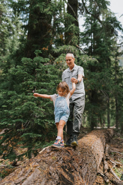 istock Granddaughter guides grandfather across a fallen tree trunk 1677397548