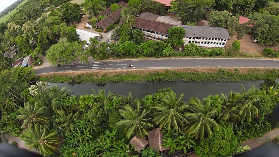 An aerial view of a rural town nestled in the countryside with a winding road lined with palm trees