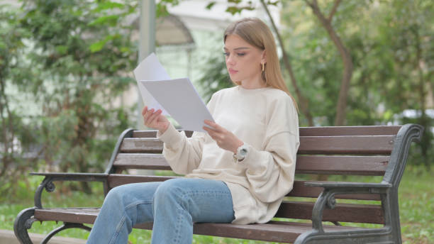 istock Casual Young Woman Reading Documents while Sitting Outdoor 1677469220