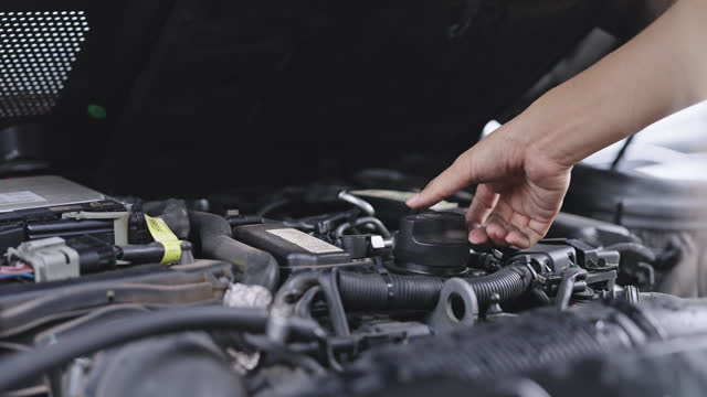 SLO MO: Close-up of woman's hand opening plastic cover under the car hood and checking the engine, radiator, and other auto parts hoping he/she can fix the car by herself after the rain.