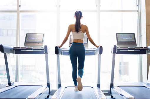 Rear view of young woman walking on treadmill