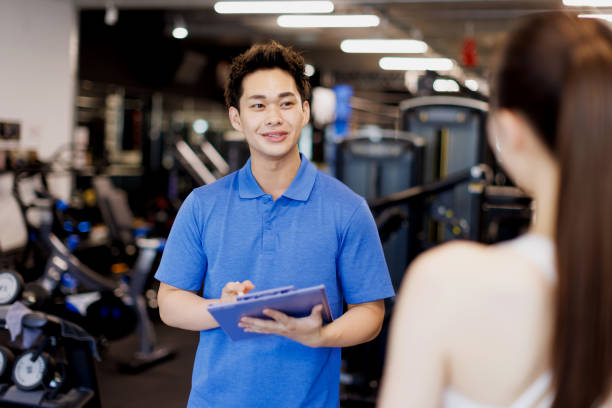 personal trainer discussing with client at gym - polo shirt two people men working imagens e fotografias de stock
