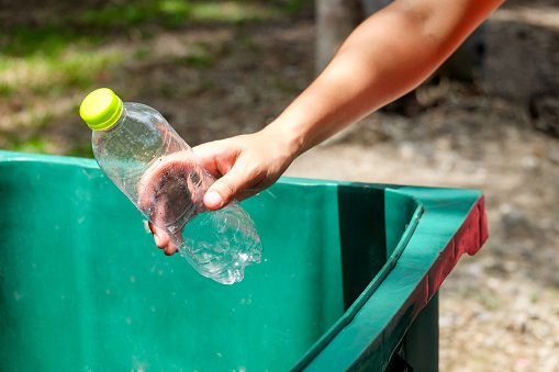 Man's hand holding a water bottle and throwing plastic bottles into the trash for disposal. Types of plastic waste and recycling. environmental concept