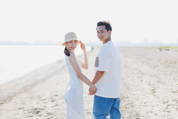 istock Young Asian couple walking by the beach with hands holding 1677544894