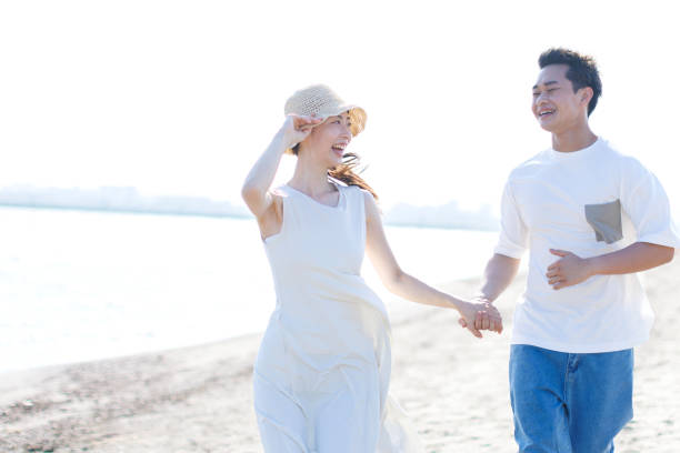 istock Young Asian couple walking by the beach with hands holding 1677545448