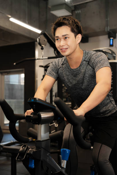 istock Young Asian man on exercise bike 1677547088
