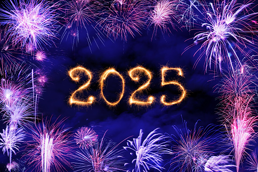 New Year fireworks and 2025 sign made of sparkler trace on a night blue sky background.
