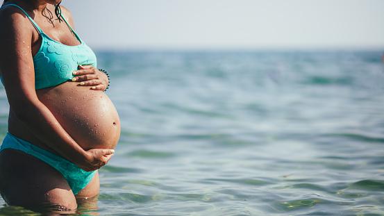 Photo of a eight month pregnant woman with hands on her abdomen at the seaside