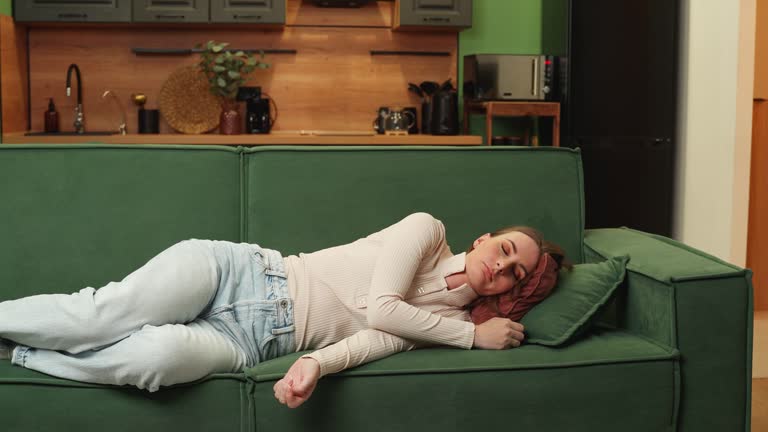 Tired young sleepy brunette woman falls on the sofa. A carefree girl is napping, falling asleep on a comfortable green sofa with pillows