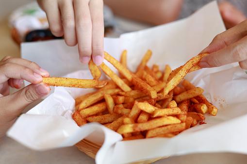 Closeup of hands taking french fries from the plate. Fried foods are cooked in oil at extremely high temperatures, they are likely to contain trans fats which associated with an increased risk of many diseases, including heart disease, cancer, diabetes and obesity.