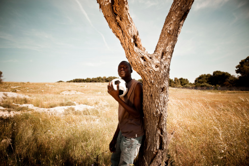 African man in the meadow, holding a soccer ball.