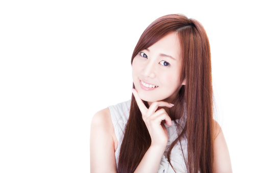 A beautiful young Japanese brunette smiling while touching her chin against a white background in studio.
