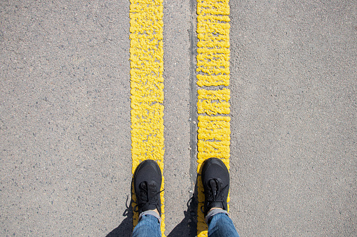 Female legs in sneakers stand on two yellow stripes on the asphalt, pointing forward, the road ahead, the path to success