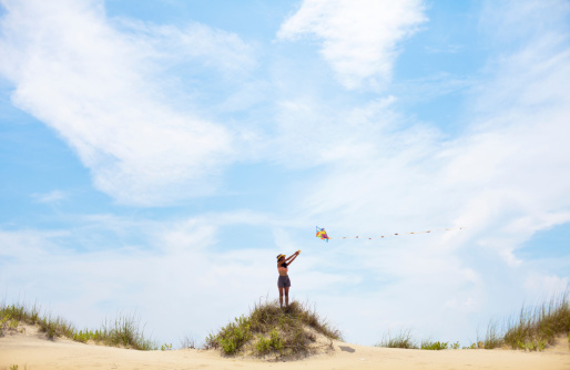 A beautiful Indian woman flying a kite from the top of a hill on a beautiful summery day at the beach in North carolina.