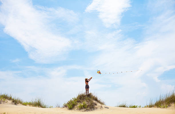 Young woman flying kite on summery day at the beach A beautiful Indian woman flying a kite from the top of a hill on a beautiful summery day at the beach in North carolina. outer banks north carolina stock pictures, royalty-free photos & images